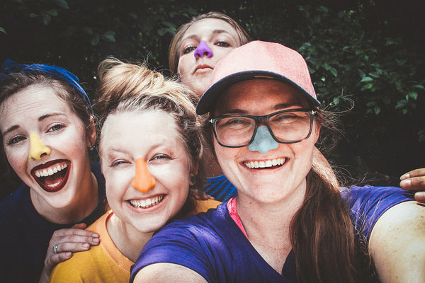 Group of four women smiling with colorful sunscreen on their nose